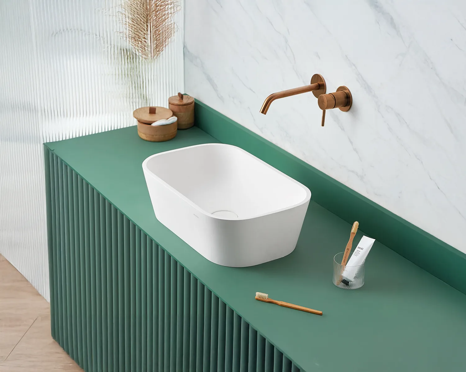 White basin on a green countertop, copper faucet, two wooden boxes, and a cup with a toothbrush and toothpaste.