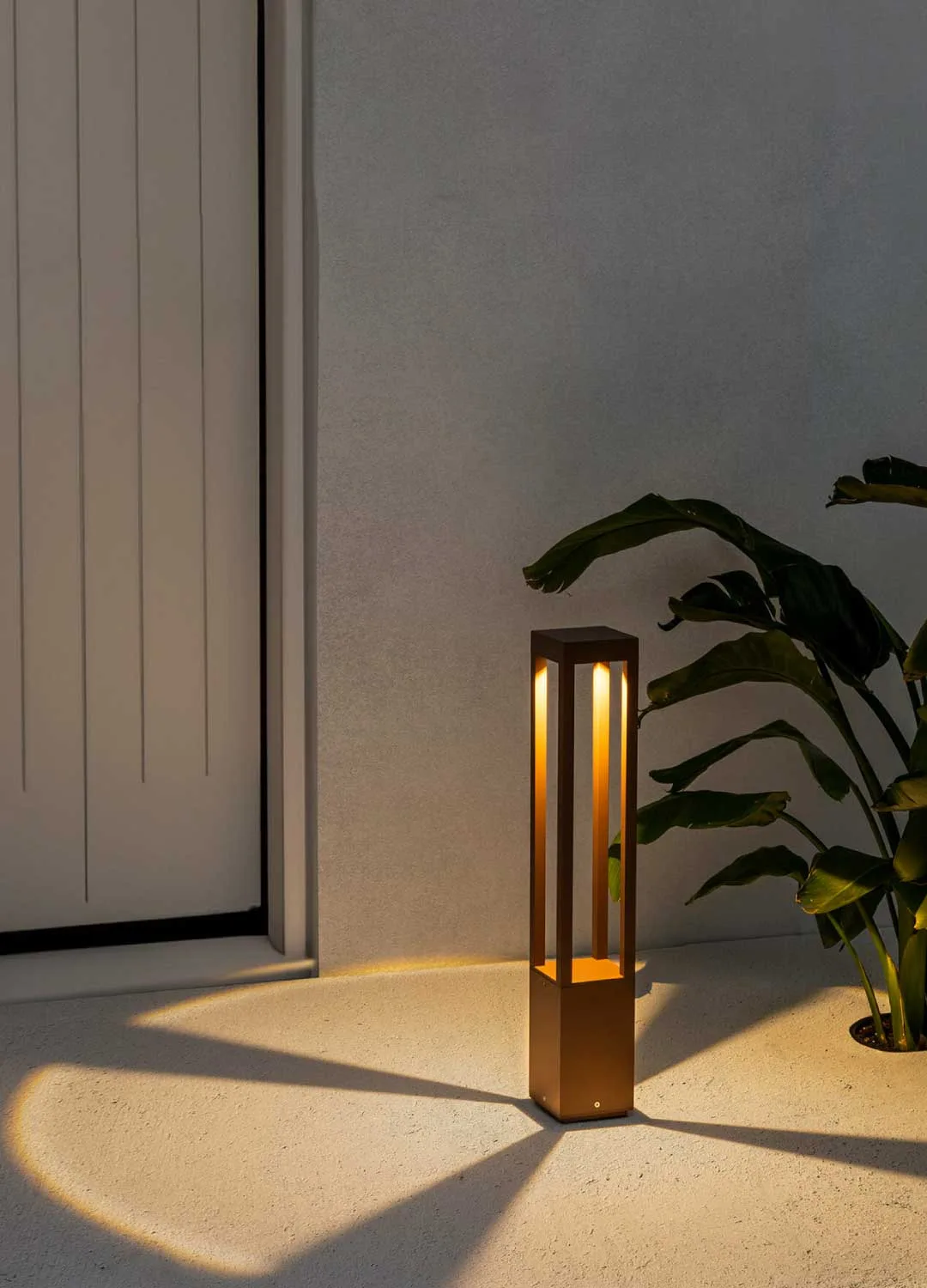 A sleek gold outdoor light softly illuminating a plant