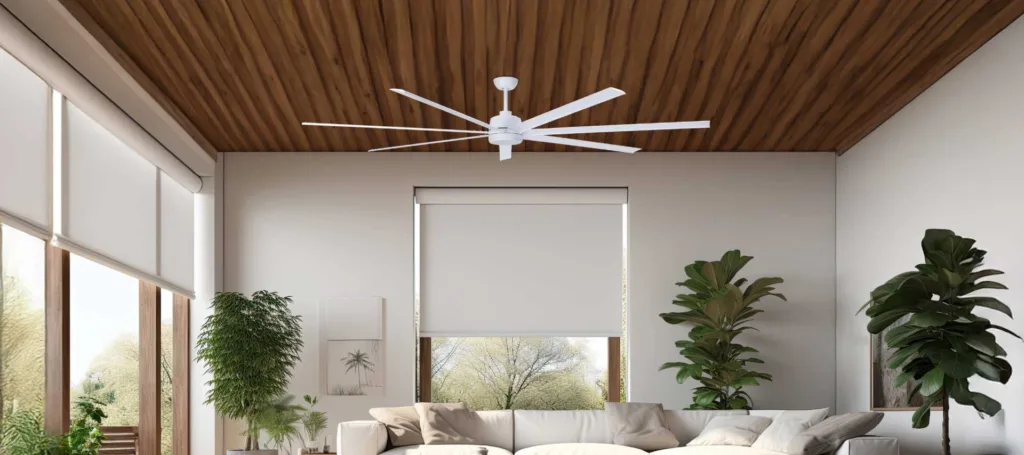 A white fan on a patio with a view of the outdoors, surrounded by green plants and trees, with a white sofa.