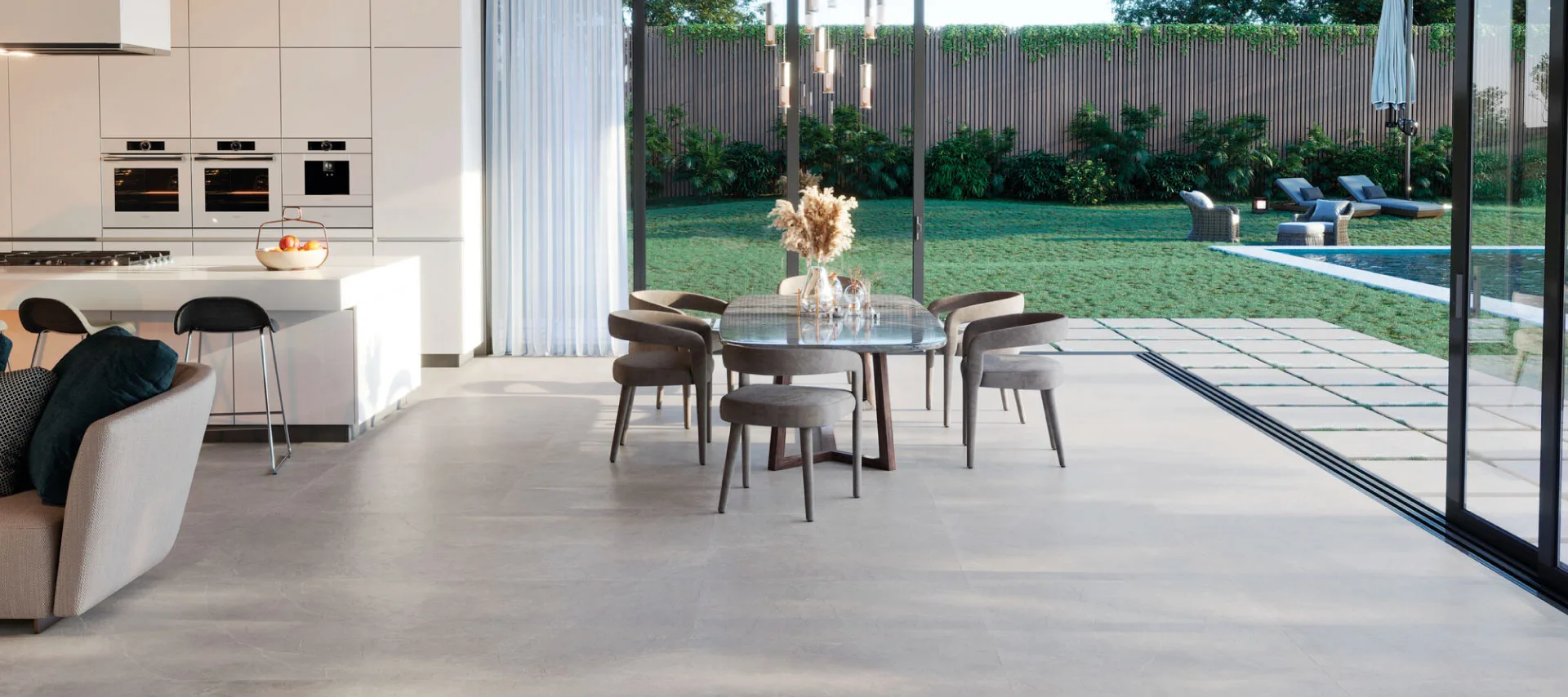 Modern living space with grey floor tiles, featuring a white kitchen with bar stools on the left, and a garden with a pool and outdoor tiles on the right.