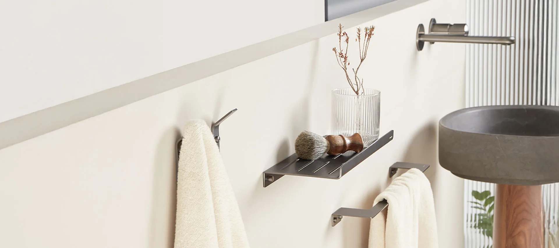 Bathroom Accessories :Modern bathroom wall with matte black towel hooks, towel bar, and shelf holding a shaving brush and glass vase, next to a concrete sink and wooden pedestal.