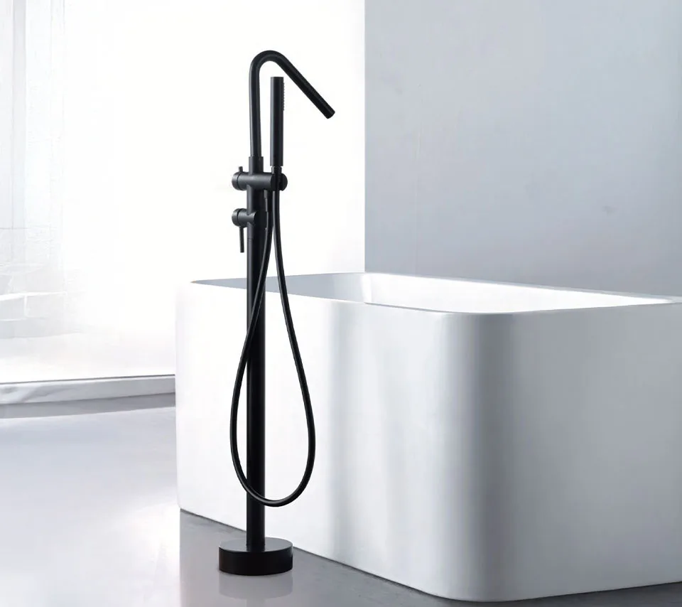 Freestanding matte black floor-mounted bathtub faucet with handheld shower next to a modern white rectangular soaking tub in a minimalist contemporary bathroom.
