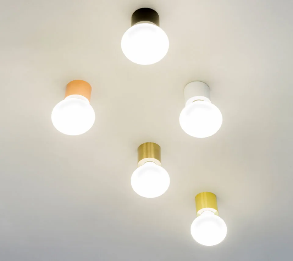 Five modern ceiling light bulbs with different colored bases – black, white, copper, gold, and yellow – mounted on a white ceiling, emitting bright, warm light.
