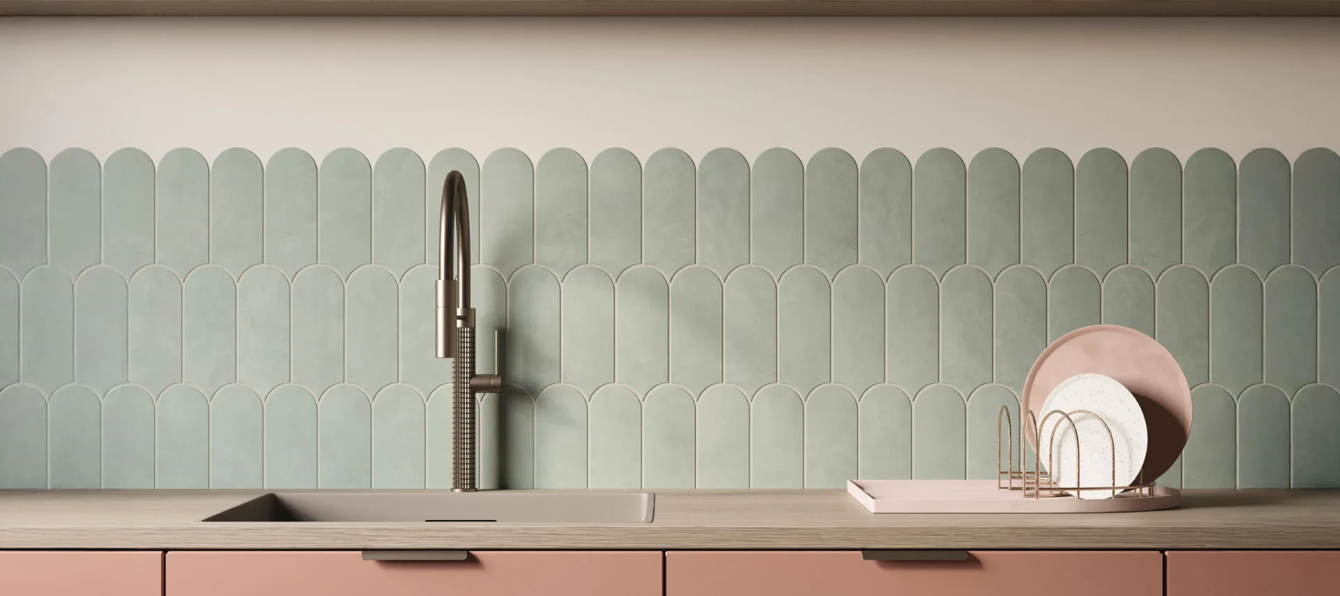 Modern kitchen with sage green scalloped ceramic tile backsplash, blush pink cabinets, light wood countertop, integrated sink, brushed metal faucet, and minimalist dish rack in a contemporary interior.