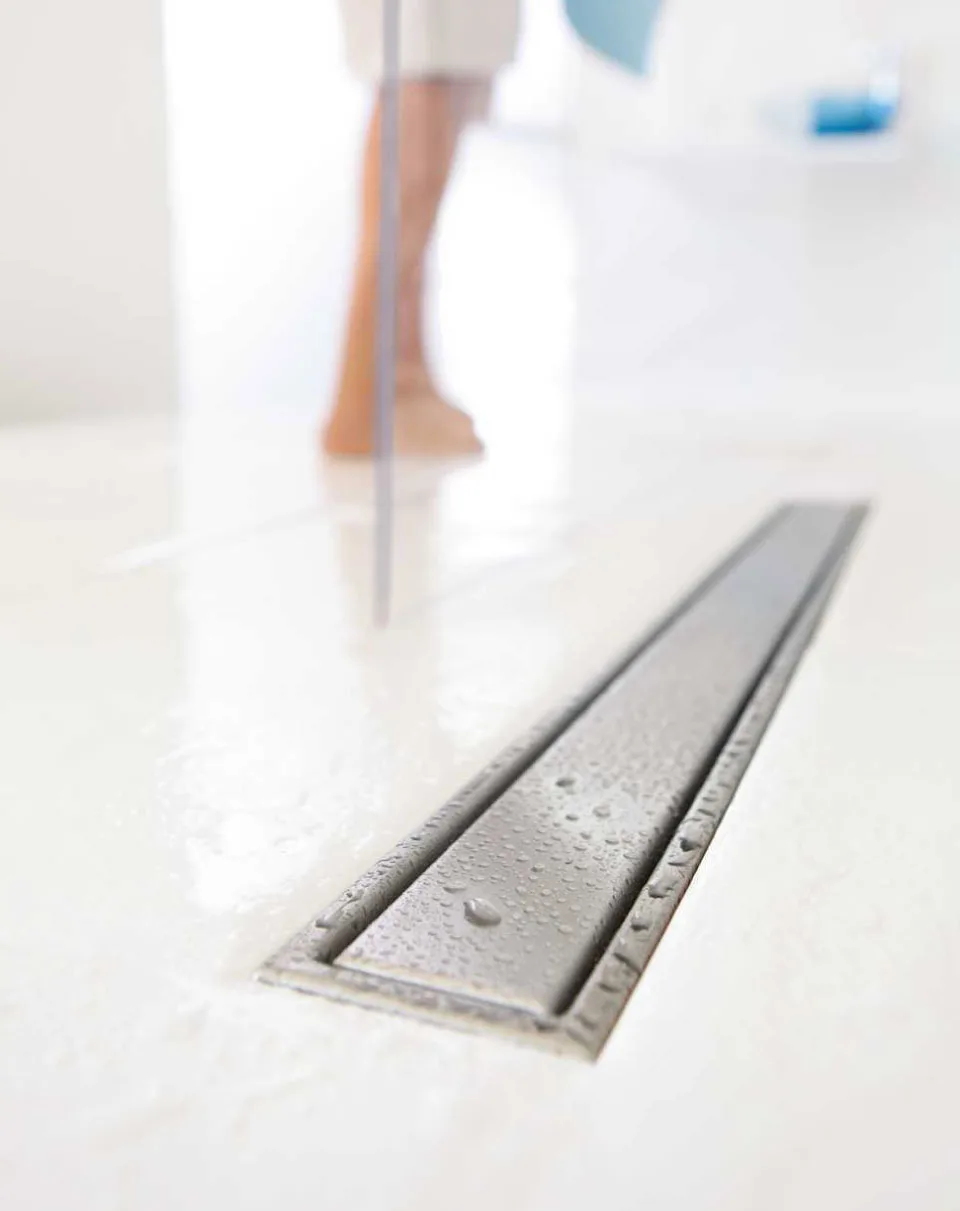 Linear shower drain in modern bathroom – sleek & efficient water management Linear shower drain in a modern bathroom floor with water droplets, showing efficient drainage system during use